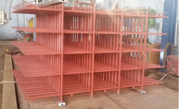 Red steel industrial rack with multi-level shelving inside a fabrication workshop.